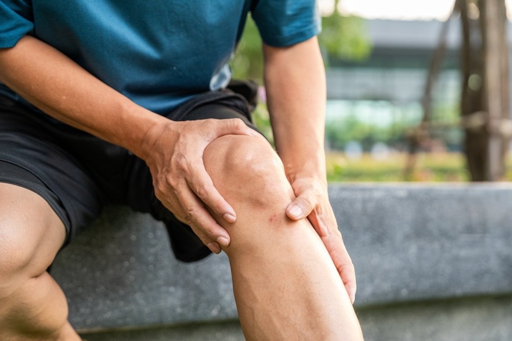 Person holding their knee in pain outdoors, illustrating chronic knee pain